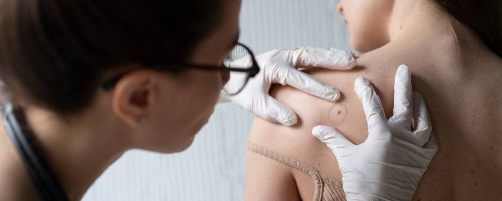 A doctor checks a woman’s back, showing the difference between skin doctors and dermatologists.