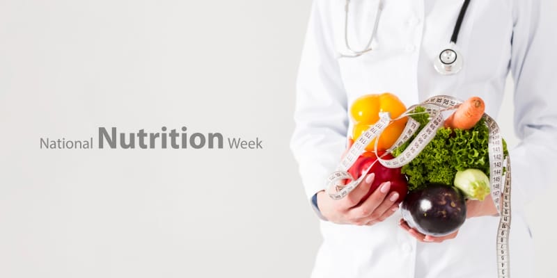 Hands gently holding a colorful assortment of fresh fruits & vegetables, representing healthy diet & National Nutrition Week.